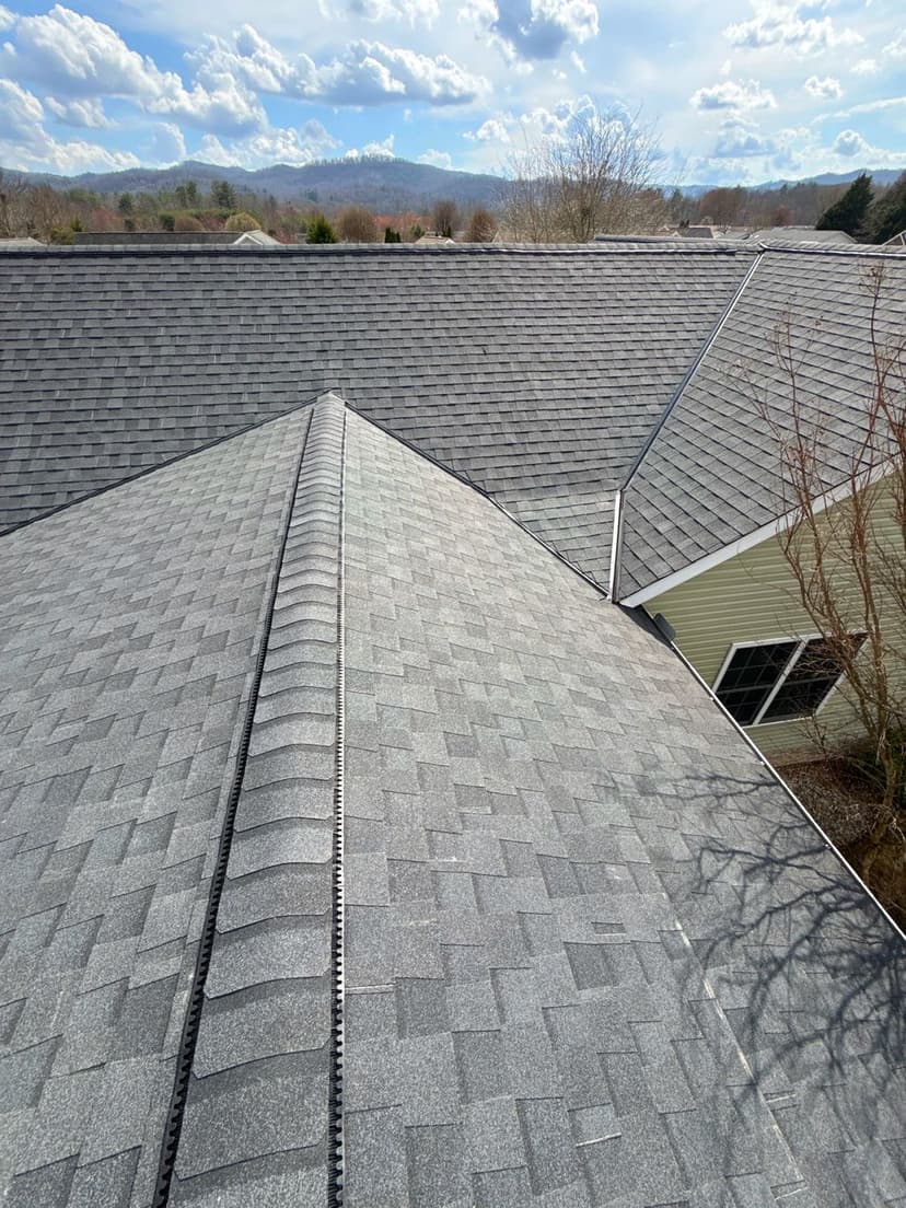 Aerial view of a modern gray shingle roof with mountains in the background.