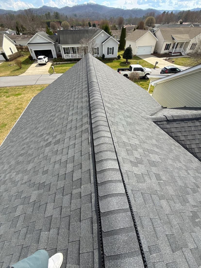 Aerial view of a gray shingle roof with ridge vent, residential neighborhood in background.
